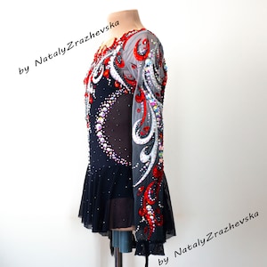 May include: A black and red figure skating dress with long sleeves, embellished with rhinestones and decorative patterns. The dress features a sheer mesh overlay and a ruffled skirt. Text on the image reads "by Nataly Zrazhevsk".