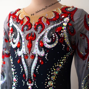 May include: A black leotard with long sheer sleeves, embellished with red and iridescent rhinestones. The design features a central pattern of silver and red accents, with the text "by Nataly Zrazhevsk" visible.