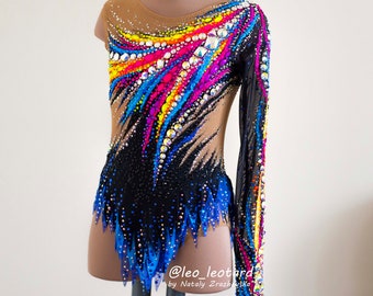 May include: A tan and black leotard with a long sleeve, embellished with colorful rhinestones and a vibrant design. The leotard features a black skirt with blue accents and a mesh sleeve. The design includes rainbow colors and is suitable for gymnastics or dance.