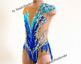 May include: A blue and tan leotard with a decorative design. The leotard features a gradient of blue hues, embellished with sparkling crystals and fringe. The shoulder is adorned with a turquoise feather-like accent. The text "by Nataly Zrazhevska" is visible.
