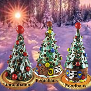 Può includere: Tre addobbi per albero di Natale in ceramica, ognuno con un design diverso. Il primo è un albero verde con accenti rossi e dorati, etichettato "Tannenbaum". Il secondo è un albero verde con un design di casa gialla e marrone, etichettato "Kegelhaus". Il terzo è un albero verde con un design di casa marrone e rossa, etichettato "Rundhaus".