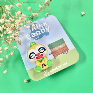 Puede incluir: Un personaje de perezoso verde y amarillo con una nariz roja y una hoja verde en su mano. El personaje está sosteniendo una fruta amarilla. El personaje está en una tarjeta blanca con el texto "Alex Candy Shoppe" y un icono de redes sociales.