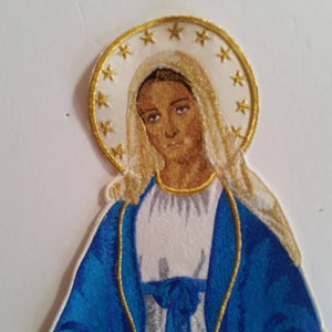 May include: Embroidered patch featuring a depiction of the Virgin Mary in a blue robe with a gold trim, holding a rosary. She is surrounded by a halo of gold stars.