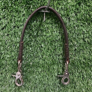 May include: A brown leather strap with silver metal clasps. The strap is hanging from a hook.