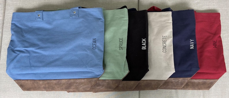 May include: Six canvas tote bags with brown leather trim. The bags are in the colors ocean, spruce, black, concrete, navy, and wine. Each bag has the color name printed on the side.