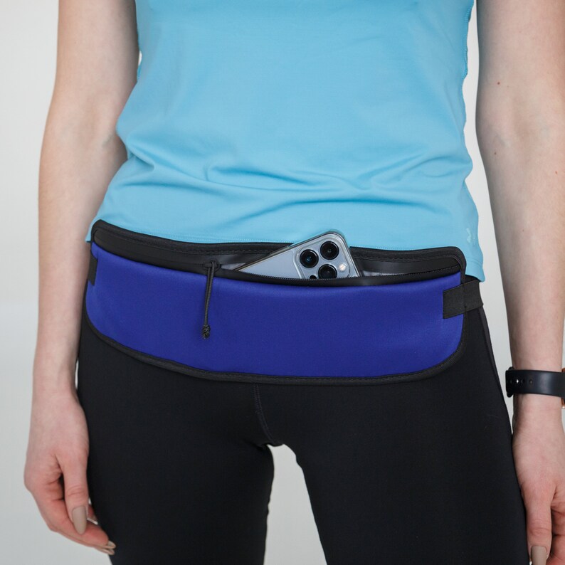 May include: A blue running belt with a black zipper and a phone pocket. The belt is worn over black leggings.