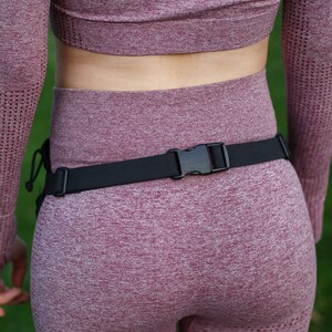 May include: A black belt with a silver buckle is worn over a pink athletic outfit. The outfit is made of a stretchy, ribbed fabric.