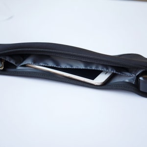 May include: A black zippered pouch with a white smartphone inside. The pouch is made of a soft, flexible material and has a zipper closure.