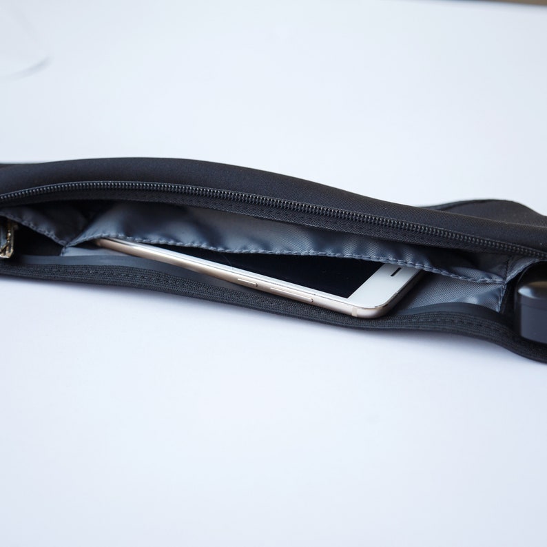 May include: A black zippered pouch with a white smartphone inside. The pouch is made of a soft, flexible material and has a zipper closure.