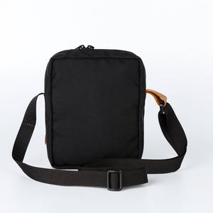May include: A black crossbody bag with a brown leather strap and a zip closure.