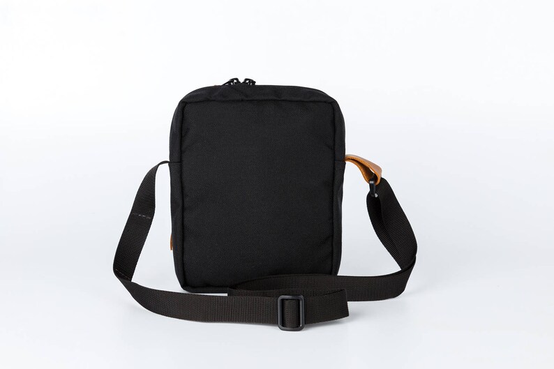 May include: A black crossbody bag with a brown leather strap and a zip closure.