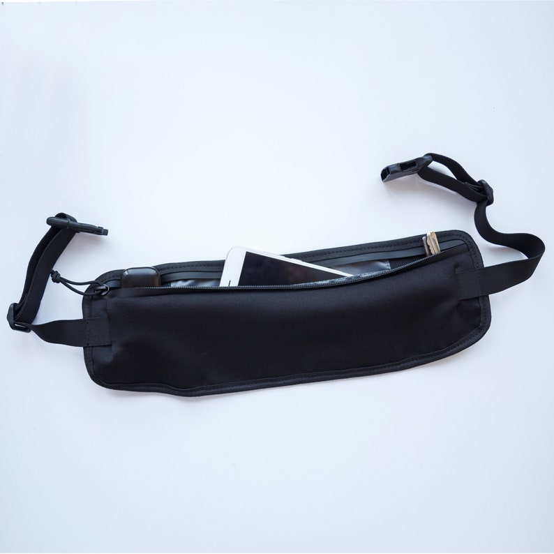 May include: A black fabric waist pack with a zippered pocket and a phone inside. The pack has an adjustable strap.