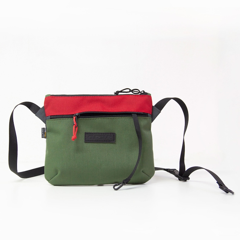 May include: A green and red crossbody bag with a black zipper and a black adjustable strap. The bag has a small black patch with the word "CURVE" on it.
