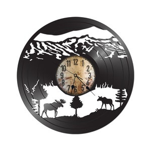 May include: Black vinyl record clock with a white silhouette of a mountain range, two moose, and trees. The clock face is in the center of the record and has black hands and white numbers.