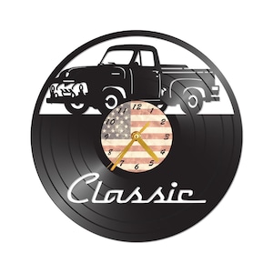 May include: Black vinyl record clock with a silhouette of a vintage pickup truck and an American flag with a clock face in the center. The clock face has gold hands and the words "Classic" are printed in white below the clock face.
