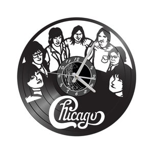 May include: Black vinyl record clock featuring a silhouette of the band Chicago. The clock face has a black background with white numbers and a silver clock hand. The band's name is written in white cursive below the clock face.
