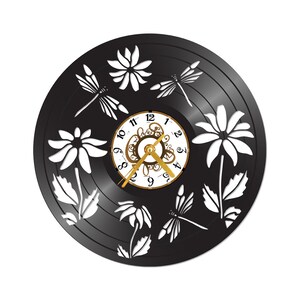 May include: A black vinyl record clock featuring white cut-out floral and dragonfly designs. The clock face is white with gold-coloured hands and numerals. The clock's design includes daisies and dragonflies.