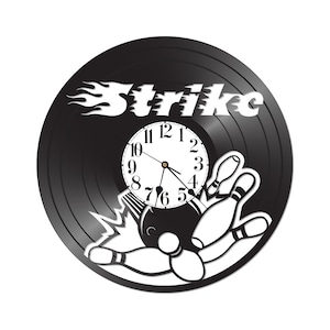 May include: Black vinyl record clock with a white bowling ball and pins design. The clock face is white with black numbers and hands. The word "Strike" is written in white with a flame design behind it.
