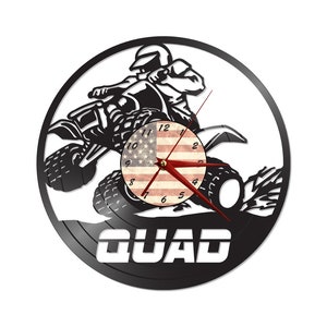 May include: Black and white wall clock featuring a silhouette of a person riding a quad bike. The clock face has an American flag design. The word "QUAD" is displayed in white block letters at the bottom of the clock.