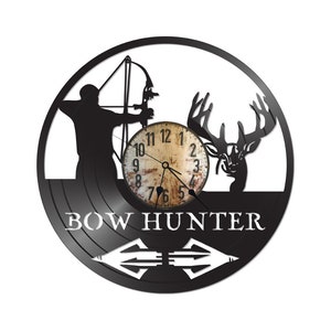 May include: Black vinyl record clock with a silhouette of a person with a bow and arrow and a deer. The clock face is white with black numbers and hands. The text "BOW HUNTER" is printed below the clock face. Two arrows are printed below the text.