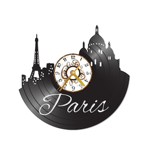 May include: A black wall clock featuring a silhouette of the Paris skyline, including the Eiffel Tower and Sacré-Cœur Basilica. The clock face is white with gold-colored hands and Roman numerals. The word "Paris" is written in a cursive font.