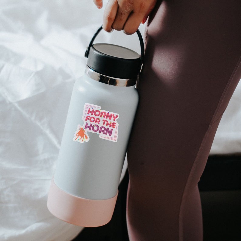 May include: A white water bottle with a pink bottom and a sticker that says "Horny for the Horn" with a cartoon unicorn in the corner.