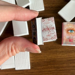 May include: A close-up of three miniature books with colorful covers. The books are titled "The Dark Mirror", "Spectacular", and "Believe Me".