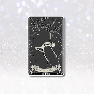 May include: A rectangular sticker with a black background features a white skeleton in a dancing pose. The words "DANCING QUEEN" are on a banner at the bottom. Stars and dotted lines decorate the background.