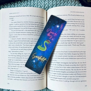 May include: A bookmark with a galaxy background and a green snake with a cowboy hat. The bookmark has the text "You go this" in neon pink letters and "Snaketet" in white letters.