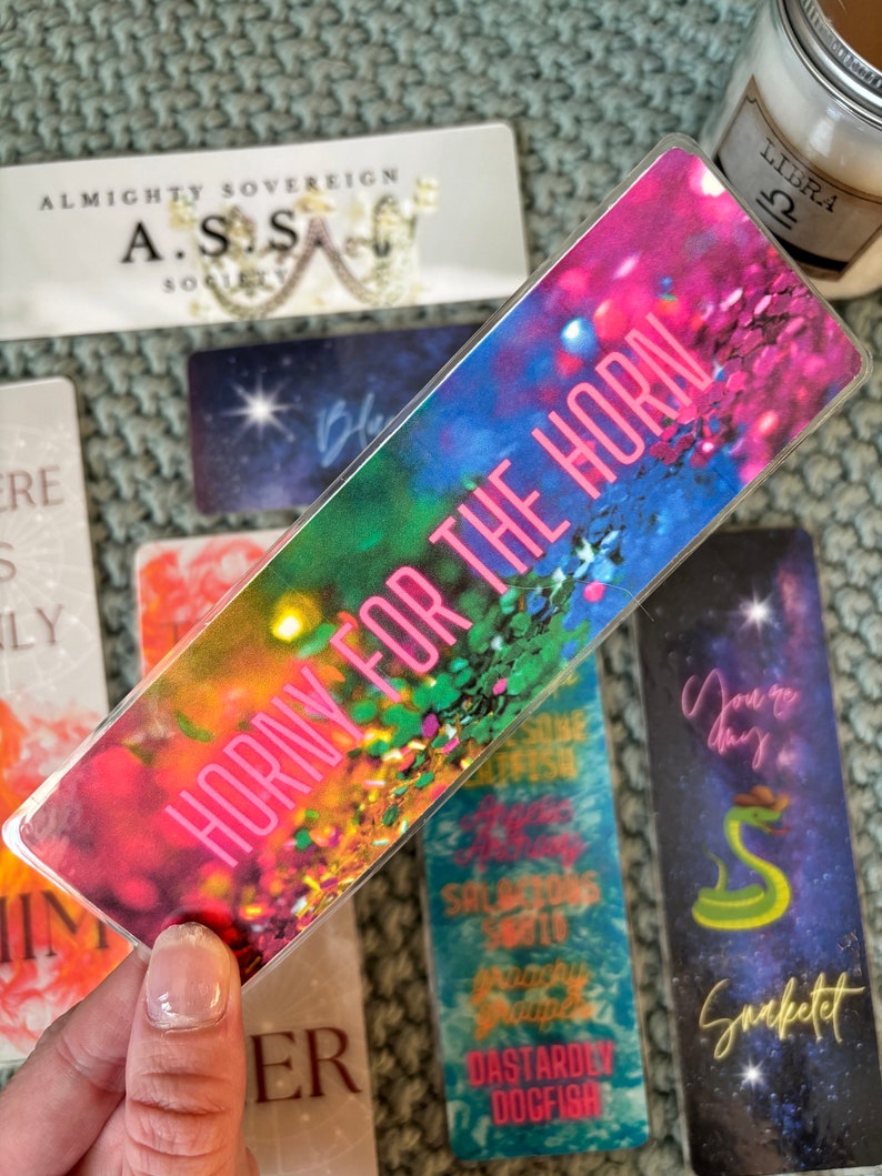 May include: A colorful bookmark with a rainbow background and the text "Horny for the Horn" in pink letters.