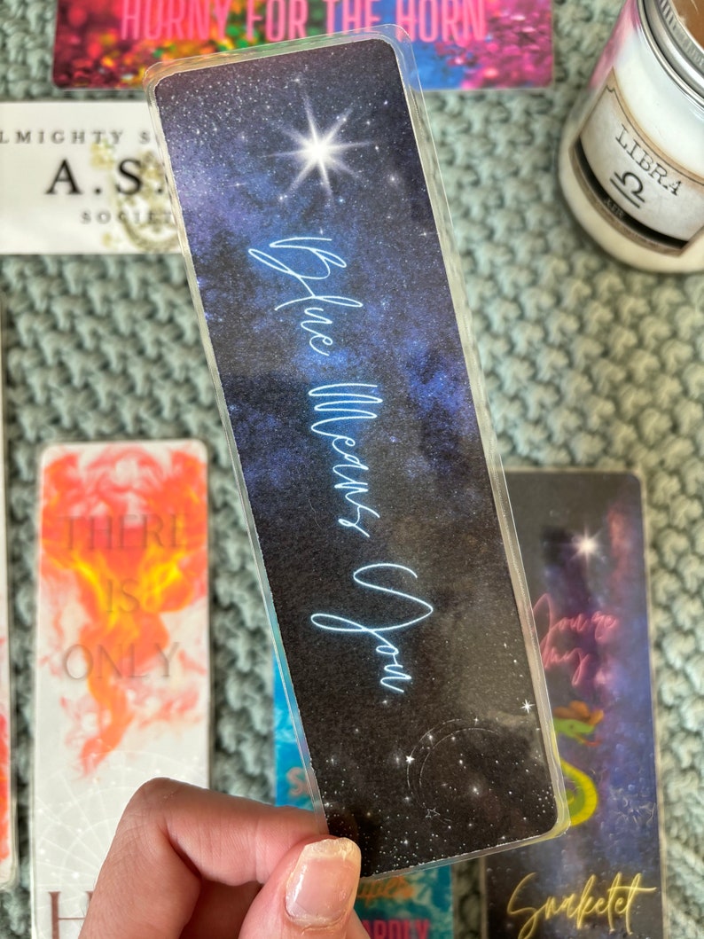 May include: A clear plastic bookmark with a galaxy design. The bookmark has a blue and white star design with the text "Blue Means You" written in white.