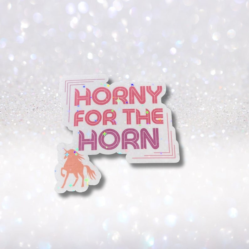 May include: A white sticker with pink and purple glitter text that reads "Horny for the Horn". A pink unicorn silhouette is below the text.