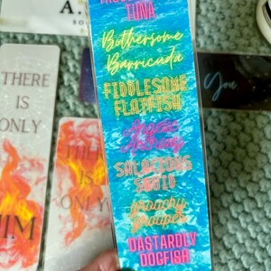 May include: A blue and white bookmark with a beach theme. The bookmark has a variety of fish names with humorous adjectives, such as "Troublesome Tuna" and "Dastardly Dogfish".