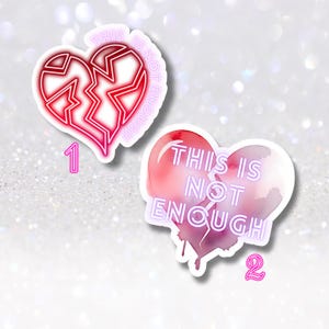 May include: Two heart-shaped stickers. One is red with a broken design and the text "THIS IS NOT ENOUGH". The other is a watercolor design with the same text. Both stickers have a white border and a number.