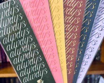 May include: A selection of bookmarks in various colours, including green, pink, yellow, brown, navy, and purple. Each bookmark features the word "always" repeated. One bookmark has a green potion bottle illustration.