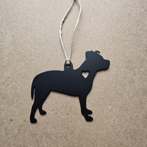 May include: Black metal ornament shaped like a pit bull dog with a small heart cutout on its chest. The ornament is hanging from a twine string.
