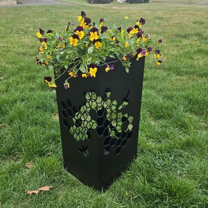May include: Black metal planter with a honeycomb design. The planter is filled with yellow and purple pansies.