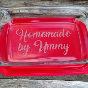 May include: A clear glass baking dish with a red lid. The dish is engraved with the text "Homemade by Ummy".