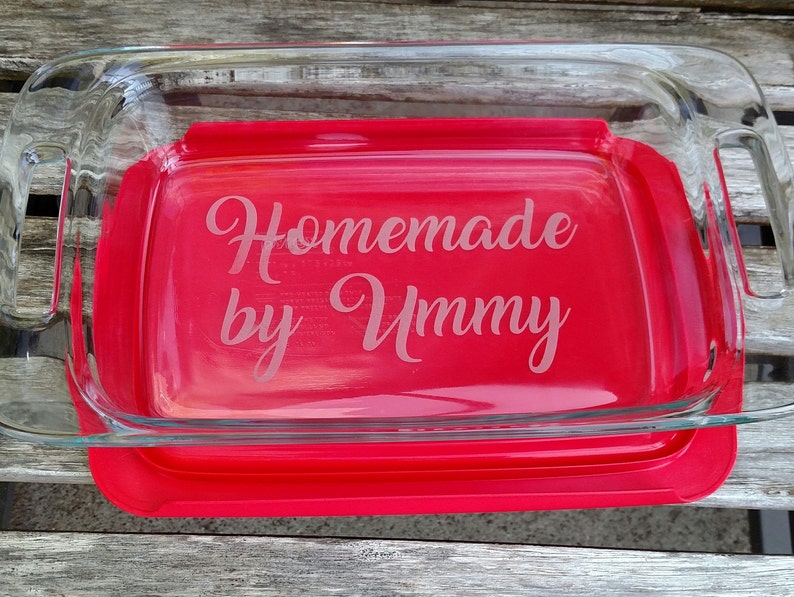 May include: A clear glass baking dish with a red lid. The dish is engraved with the text "Homemade by Ummy".