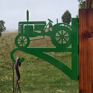 May include: Green metal tractor silhouette wall hook with a decorative scroll design. The hook is mounted on a wooden post and is suitable for hanging plants or other items.