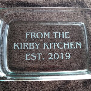 May include: A clear glass baking dish with two handles. The dish is engraved with the text "From the Kirby Kitchen Est. 2019".