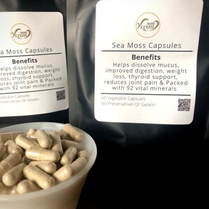 May include: Two black bags of sea moss capsules with white labels. The labels have the text "TASTED Vegan" and "Sea Moss Capsules". The labels also list the benefits of sea moss, which include helping to dissolve mucus, improving digestion, aiding in weight loss, supporting thyroid health, reducing joint pain, and providing 92 vital minerals. The bags are labeled with "60 Vegetable Capsules" and "No Preservatives Or Gelatin". A white bowl filled with sea moss capsules is in the foreground.