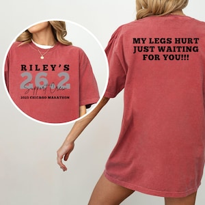 May include: A red t-shirt with the text "RILEY'S 26.2 Support Crew 2025 Chicago Marathon" on the front. The back of the shirt says "MY LEGS HURT JUST WAITING FOR YOU!!!". The shirt is a comfortable, casual style.