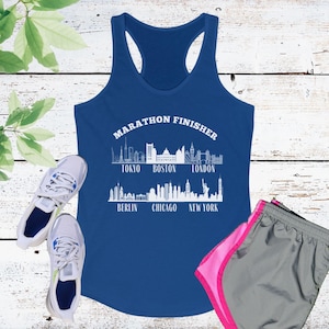 May include: A blue racerback tank top with the text "MARATHON FINISHER" and city skylines. Includes white sneakers and gray running shorts with pink trim. The tank top features the skylines of Tokyo, Boston, London, Berlin, Chicago, and New York.