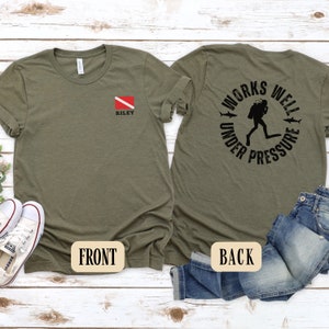 May include: A green t-shirt with a scuba diving flag on the front and the text "WORKS WELL UNDER PRESSURE" with a scuba diver graphic on the back.