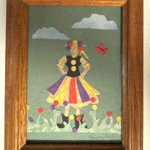 Pu&ograve; includere: Un collage di carta incorniciato con una figura con un top nero, una gonna colorata e stivali neri. L'opera d'arte include uno sfondo verde, nuvole blu, una farfalla rossa e punti colorati. La cornice &egrave; in legno.
