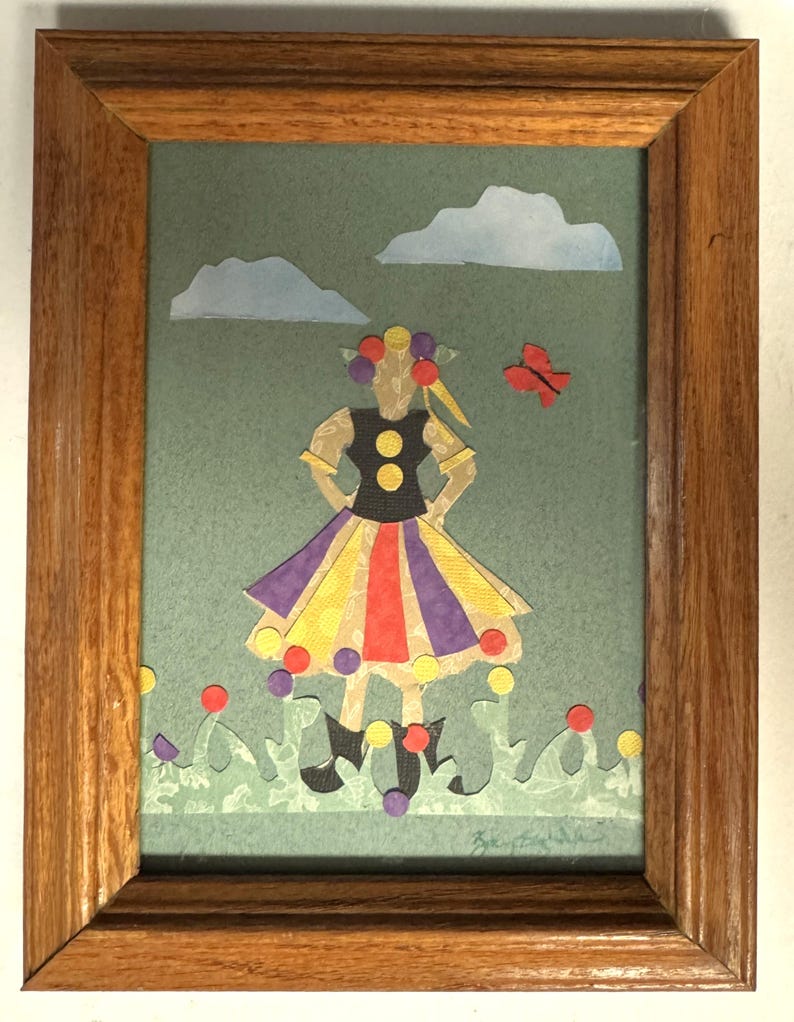 Pu&ograve; includere: Un collage di carta incorniciato con una figura con un top nero, una gonna colorata e stivali neri. L'opera d'arte include uno sfondo verde, nuvole blu, una farfalla rossa e punti colorati. La cornice &egrave; in legno.