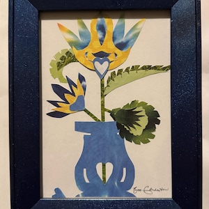 Pu&ograve; includere: Un'opera d'arte floreale incorniciata. L'opera presenta un vaso blu con un ritaglio a forma di cuore, che tiene un fiore con petali gialli e blu. La cornice &egrave; blu scuro e l'opera &egrave; firmata.