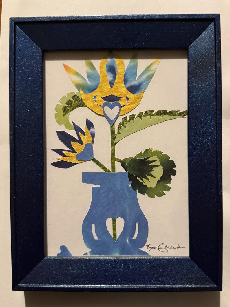 Pu&ograve; includere: Un'opera d'arte floreale incorniciata. L'opera presenta un vaso blu con un ritaglio a forma di cuore, che tiene un fiore con petali gialli e blu. La cornice &egrave; blu scuro e l'opera &egrave; firmata.