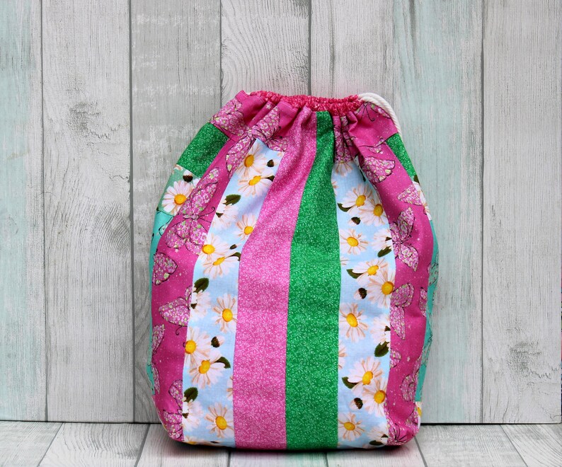 May include: A pink and green drawstring bag with a floral and butterfly print. The bag is made of fabric and has a white drawstring.